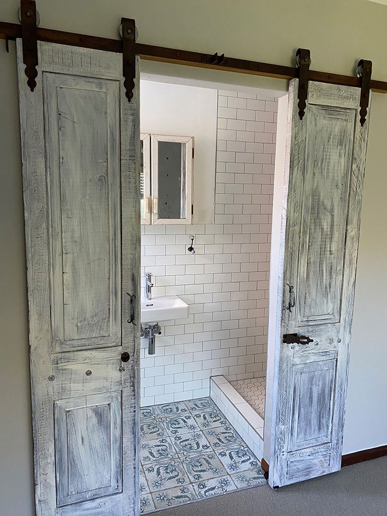 Whitewashed distressed double barn doors opening to a tiled bathroom